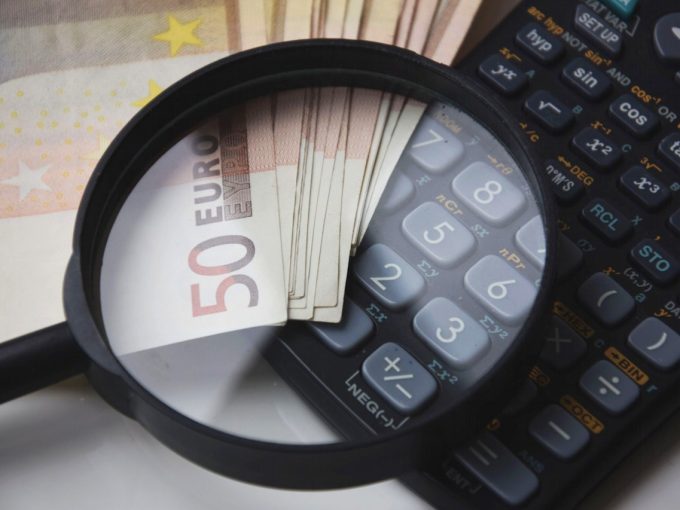 lente di ingrandimento su banconote e calcolatrice per focus su spese di registrazione contratto di locazione